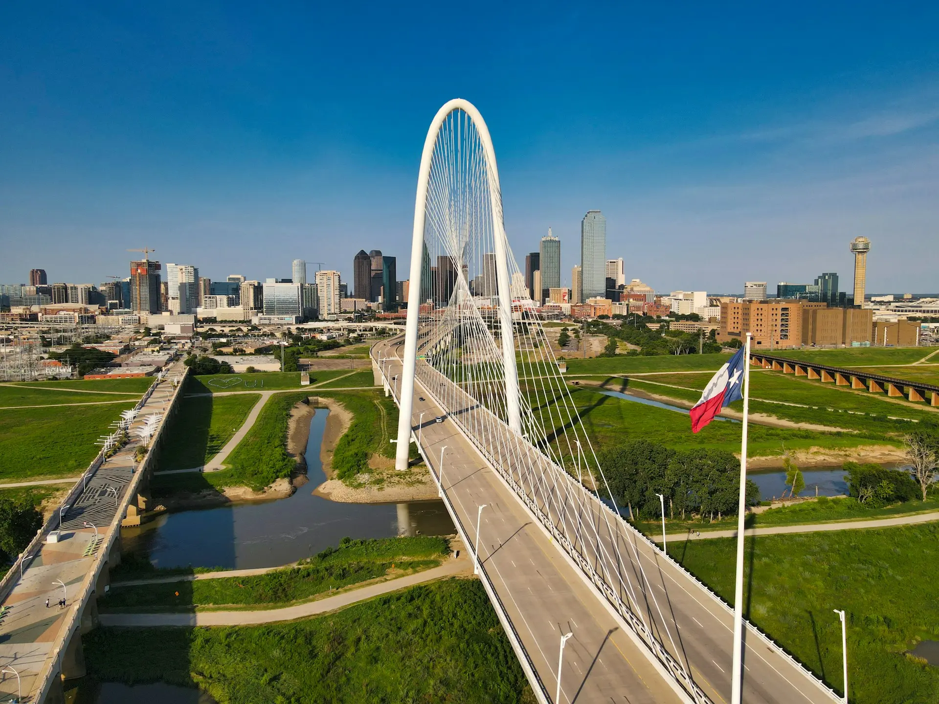 The white arch of the bridge over the Trinity River, with downtown Dallas behind it